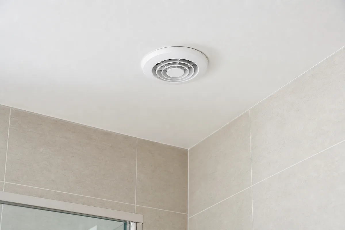 Grille d’extraction de VMC blanche fixée au plafond d’une salle de bains carrelée